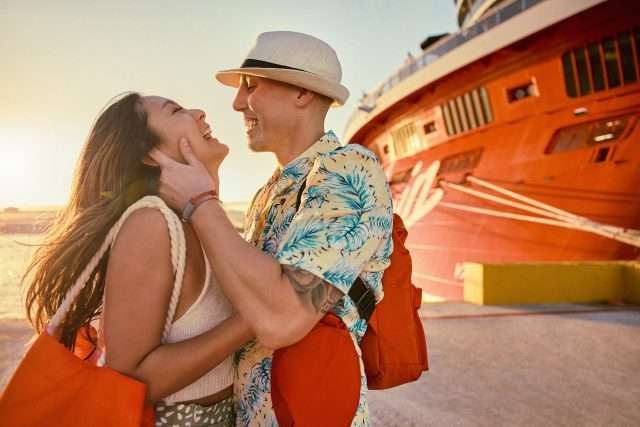 A couple smiles in front of the aft of Valiant Lady during sunset. Lifestyle imagery
