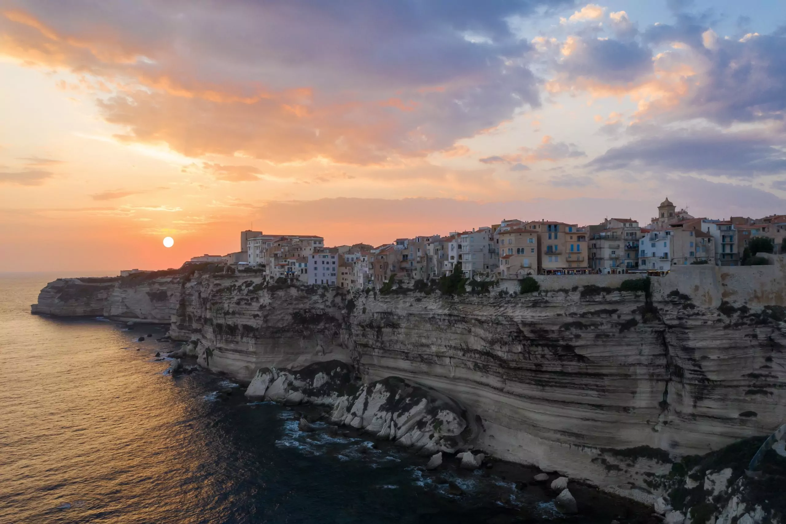 A village on a cliff over the ocean with the sunset in the background